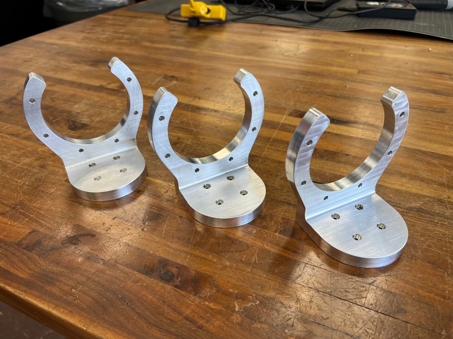 Three CNC-milled aluminum joint brackets on a wooden bench