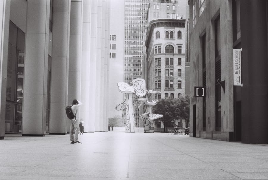 Black-and-white photo of a lone figure in a plaza between tall columns