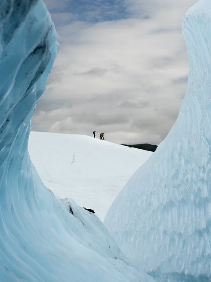 Two climbers on the rim of a blue glacier ice formation