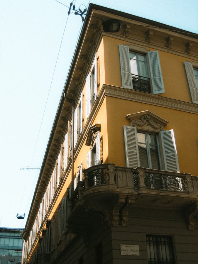 Ochre building corner with green shutters against a pale sky