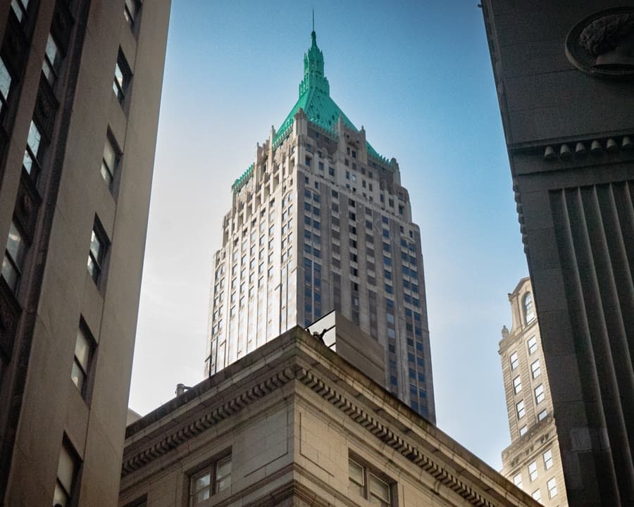 Looking up at a green-topped skyscraper between neighboring buildings