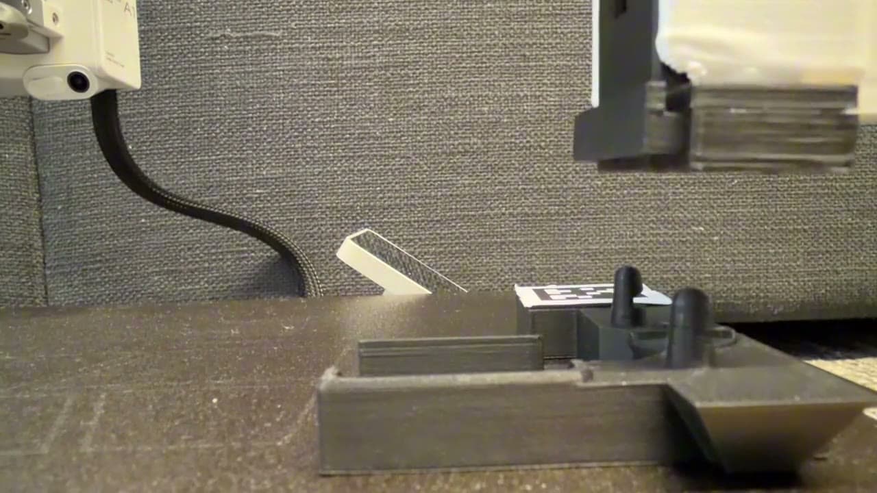 The wrist lowering onto a printed tool marked with an AprilTag